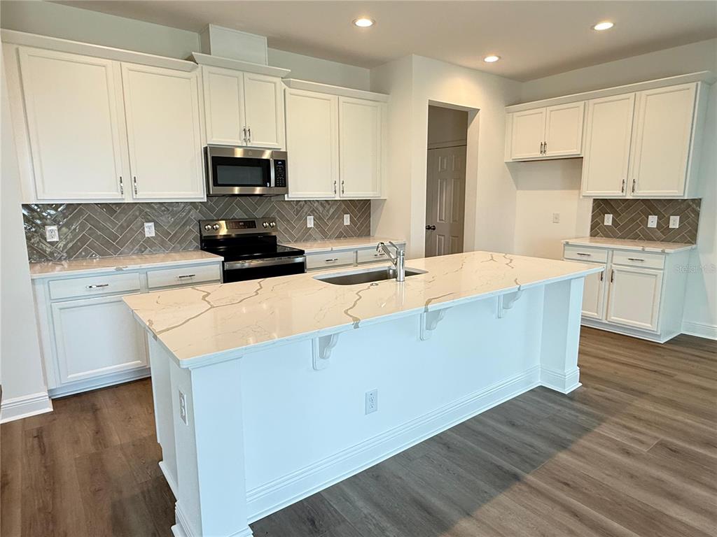 A modern kitchen features white cabinets, a large quartz island, and a herringbone tile backsplash — 7497 CATANIA LOOP, CLERMONT, FL