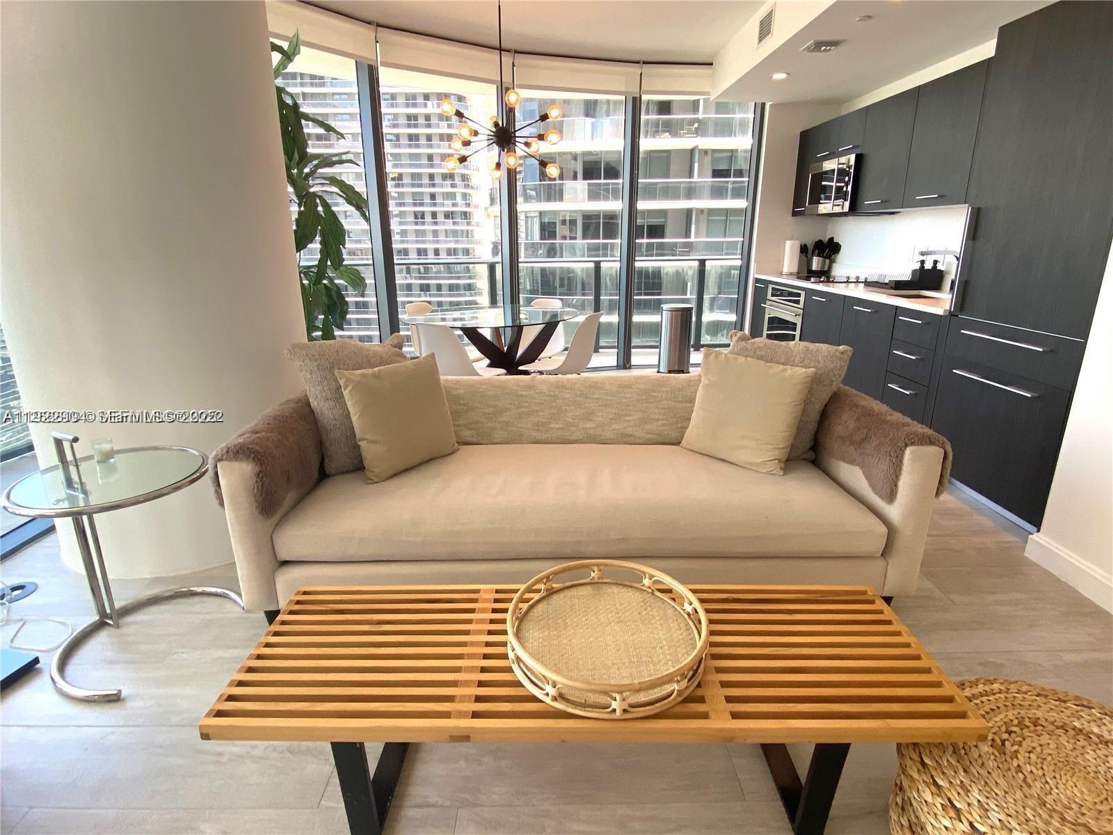 A modern living room features a beige sofa, a slatted coffee table, and floor-to-ceiling windows — 55 SW 9th St # 3001, Miami FL 33130, MIAMI, FL
