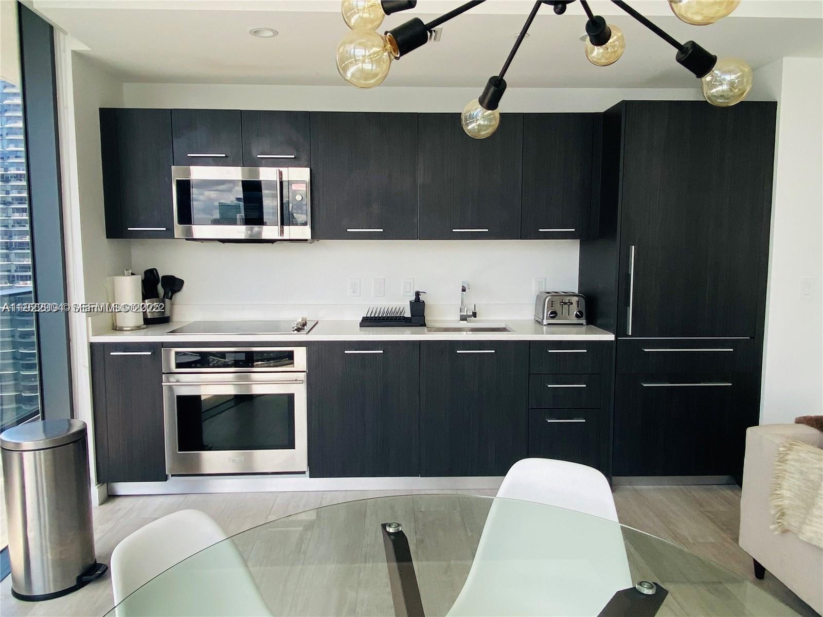 A modern kitchen features dark wood cabinets, stainless steel appliances, and a white countertop — 55 SW 9th St # 3001, Miami FL 33130, MIAMI, FL