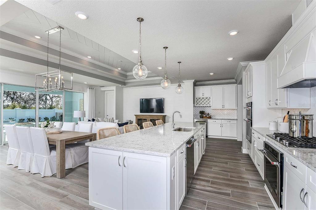 A bright, open-concept kitchen features white cabinetry, a large quartz island, and wood-look tile flooring — 9030 WANDER TRAIL, MELBOURNE, FL