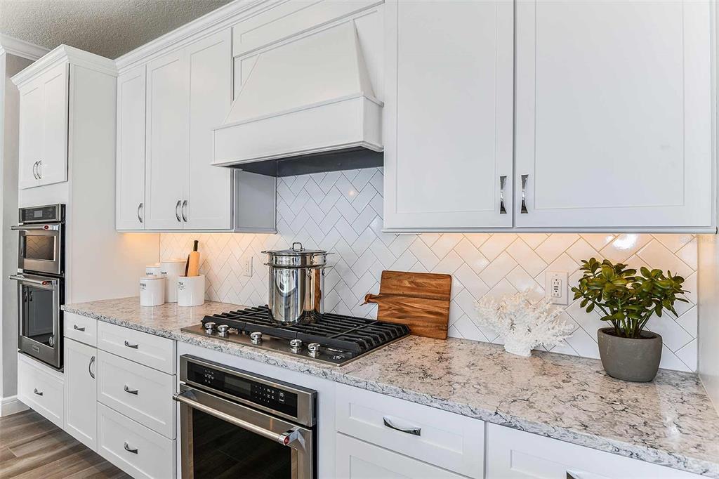 A kitchen features white cabinets, a herringbone tile backsplash, granite countertops, and stainless steel appliances — 9030 WANDER TRAIL, MELBOURNE, FL