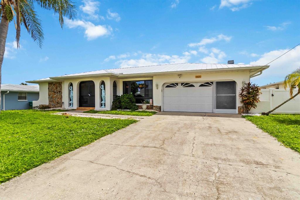 A single-story house with a white metal roof, a two-car garage, and a concrete driveway — 18606 BRIGGS CIRCLE, PORT CHARLOTTE, FL