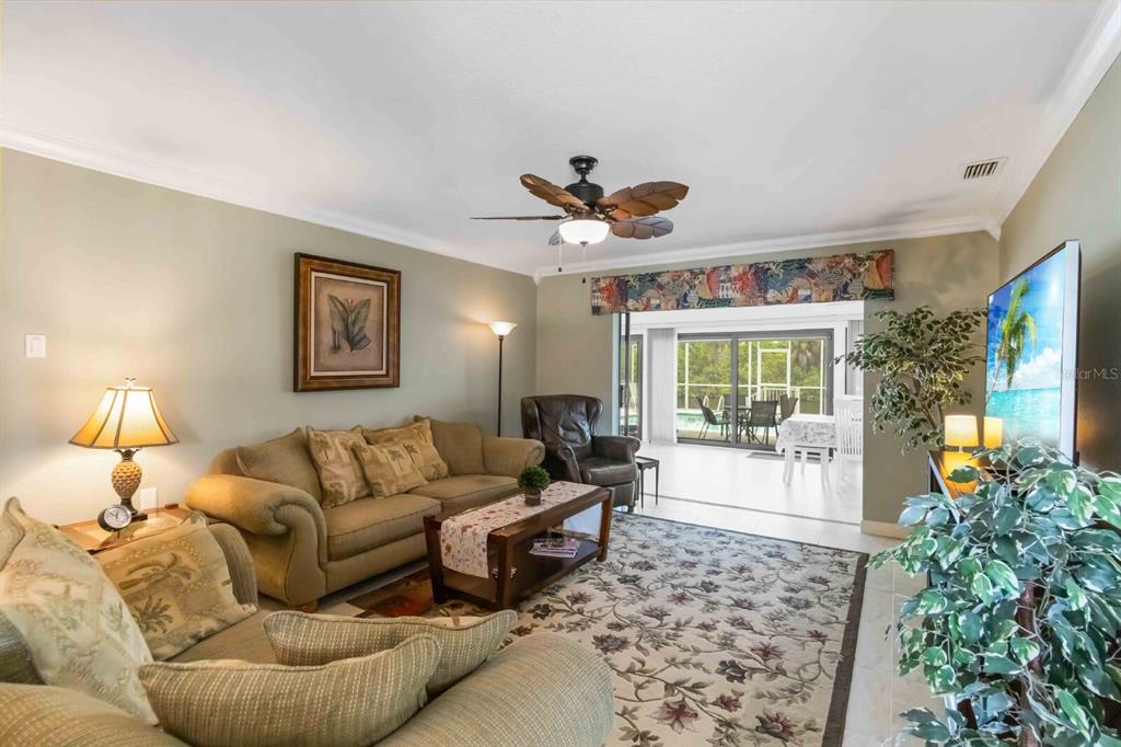 A living room with a beige sofa, patterned rug, ceiling fan, and sliding glass doors — 18606 BRIGGS CIRCLE, PORT CHARLOTTE, FL