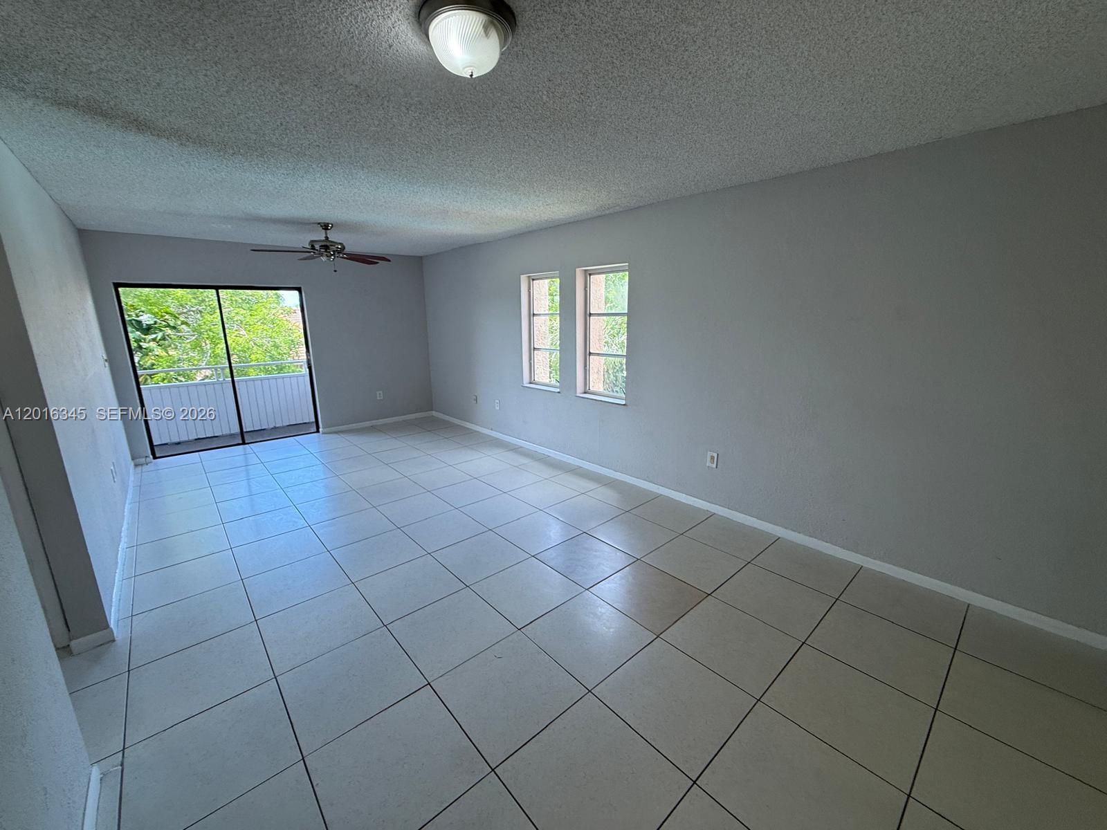 An empty living room features light gray walls, white tile flooring, and a sliding glass door — 17530 NW 68th Ave # C3004, Hialeah FL 33015, HIALEAH, FL