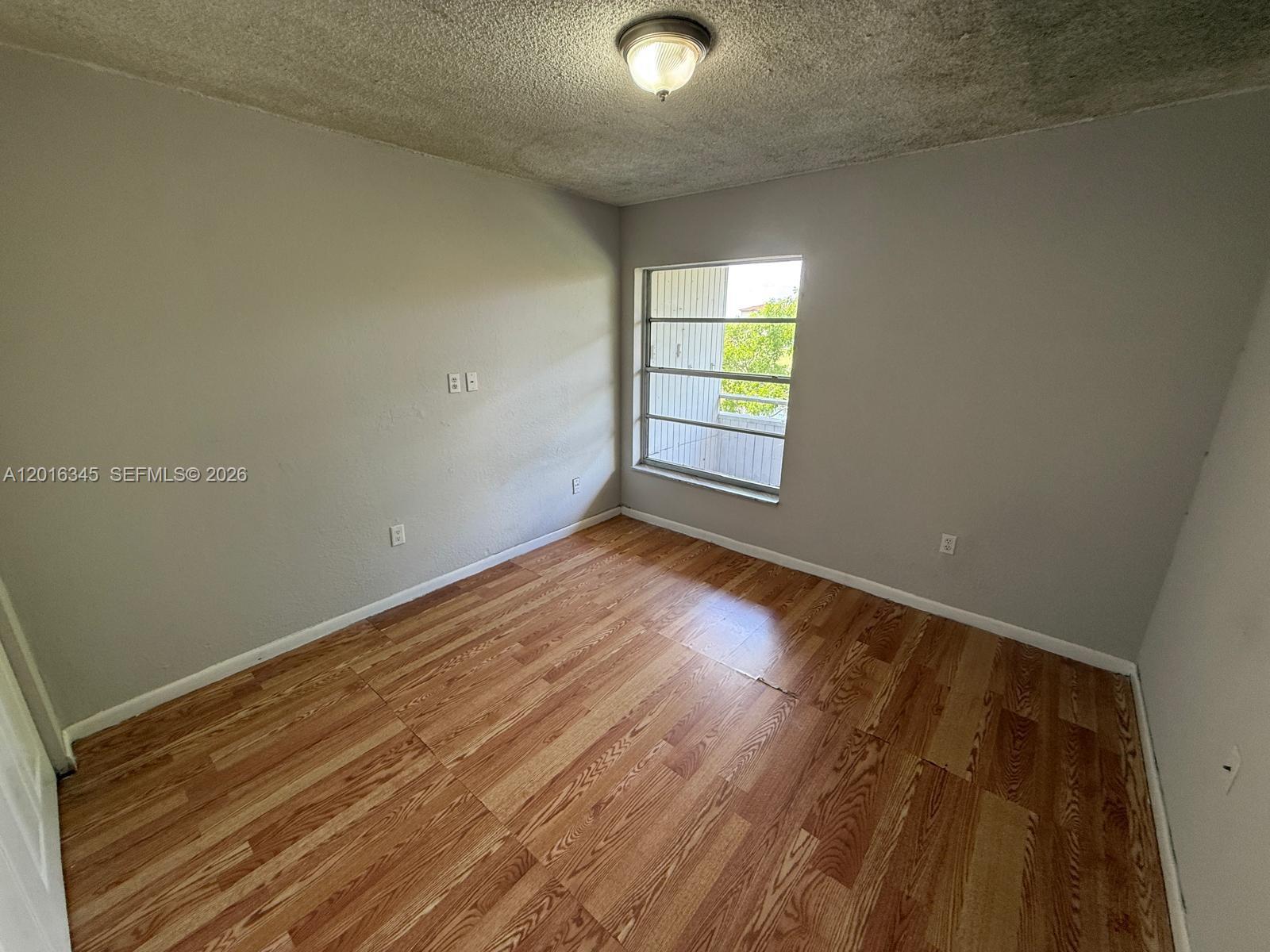 An empty room features light gray walls, wood-look flooring, a popcorn ceiling, and one window — 17530 NW 68th Ave # C3004, Hialeah FL 33015, HIALEAH, FL
