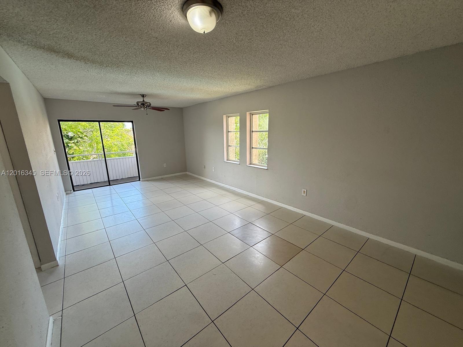 An empty living room features light-colored tile flooring, gray walls, and a sliding glass door — 17530 NW 68th Ave # C3004, Hialeah FL 33015, HIALEAH, FL