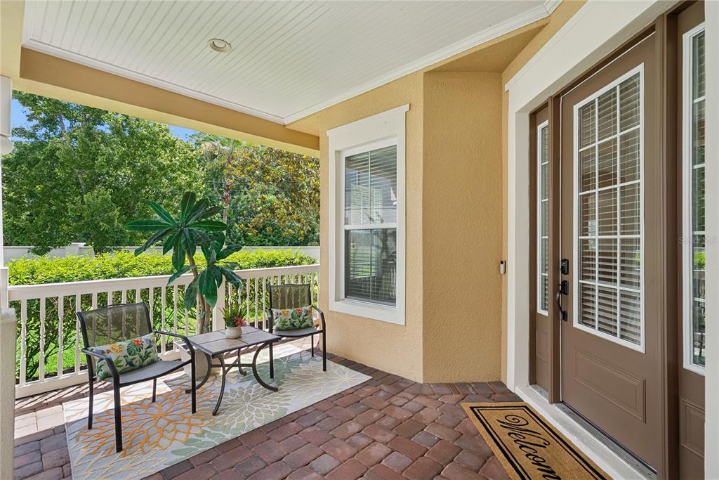A covered porch features a brick floor, two chairs, a small table, and a front door — 3600 SIMONTON PLACE, LAKE MARY, FL