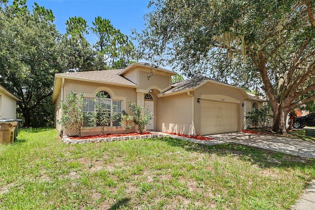 A single-story house with a beige stucco exterior, a two-car garage, and mature trees — 3709 CINNAMON FERN LOOP, CLERMONT, FL