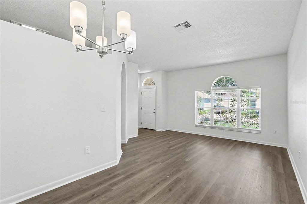 A bright, empty room features white walls, wood-look flooring, a chandelier, and a front door — 3709 CINNAMON FERN LOOP, CLERMONT, FL