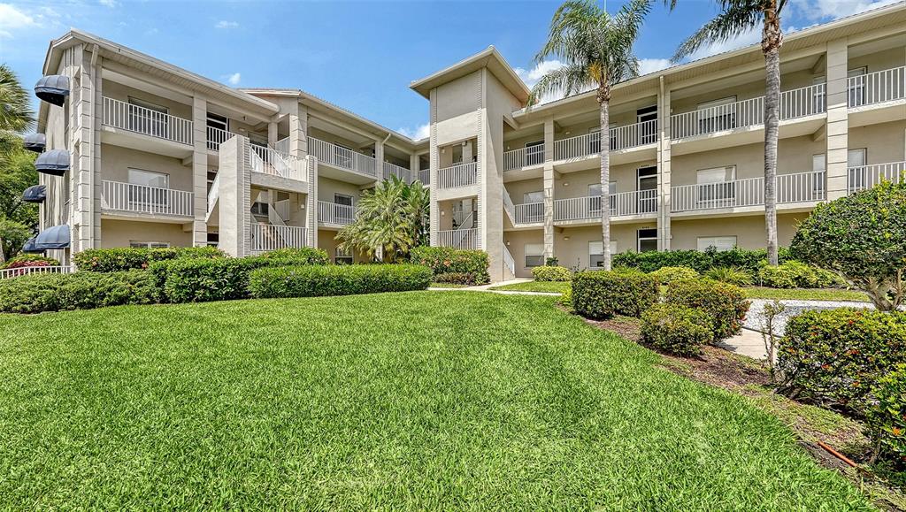 A multi-story apartment building features beige stucco walls, white railings, and a manicured lawn — 9630 CLUB SOUTH CIRCLE UNIT 6202, SARASOTA, FL