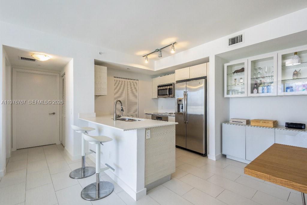 A modern kitchen features white cabinetry, stainless steel appliances, a breakfast bar, and tile flooring — 4250 Biscayne Blvd # 816, Miami FL 33137, MIAMI, FL
