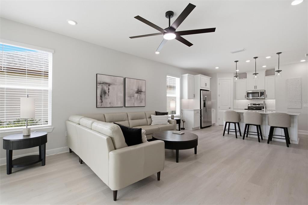 A modern open-concept living room and kitchen feature light wood flooring and white cabinetry — 1369 LOMBARDI COURT, POINCIANA, FL