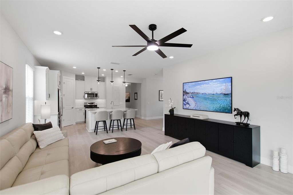 A modern open-concept living room features a white sectional sofa, a black media console, and kitchen — 1369 LOMBARDI COURT, POINCIANA, FL