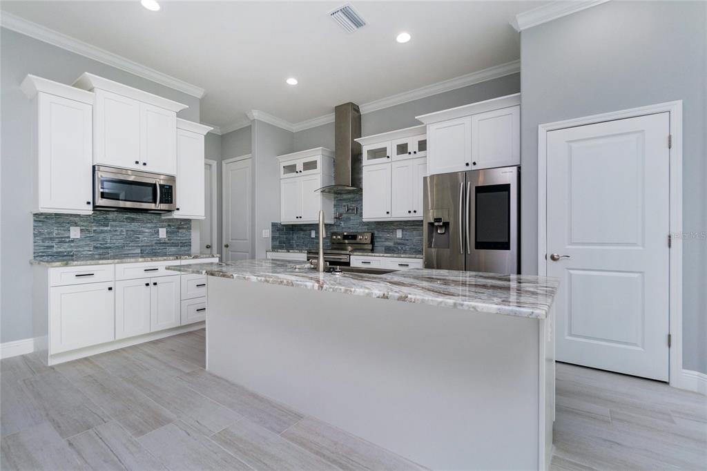 A modern kitchen features white cabinetry, a marble-topped island, stainless steel appliances, and blue backsplash — 13344 GERSHWIN LANE, PORT CHARLOTTE, FL