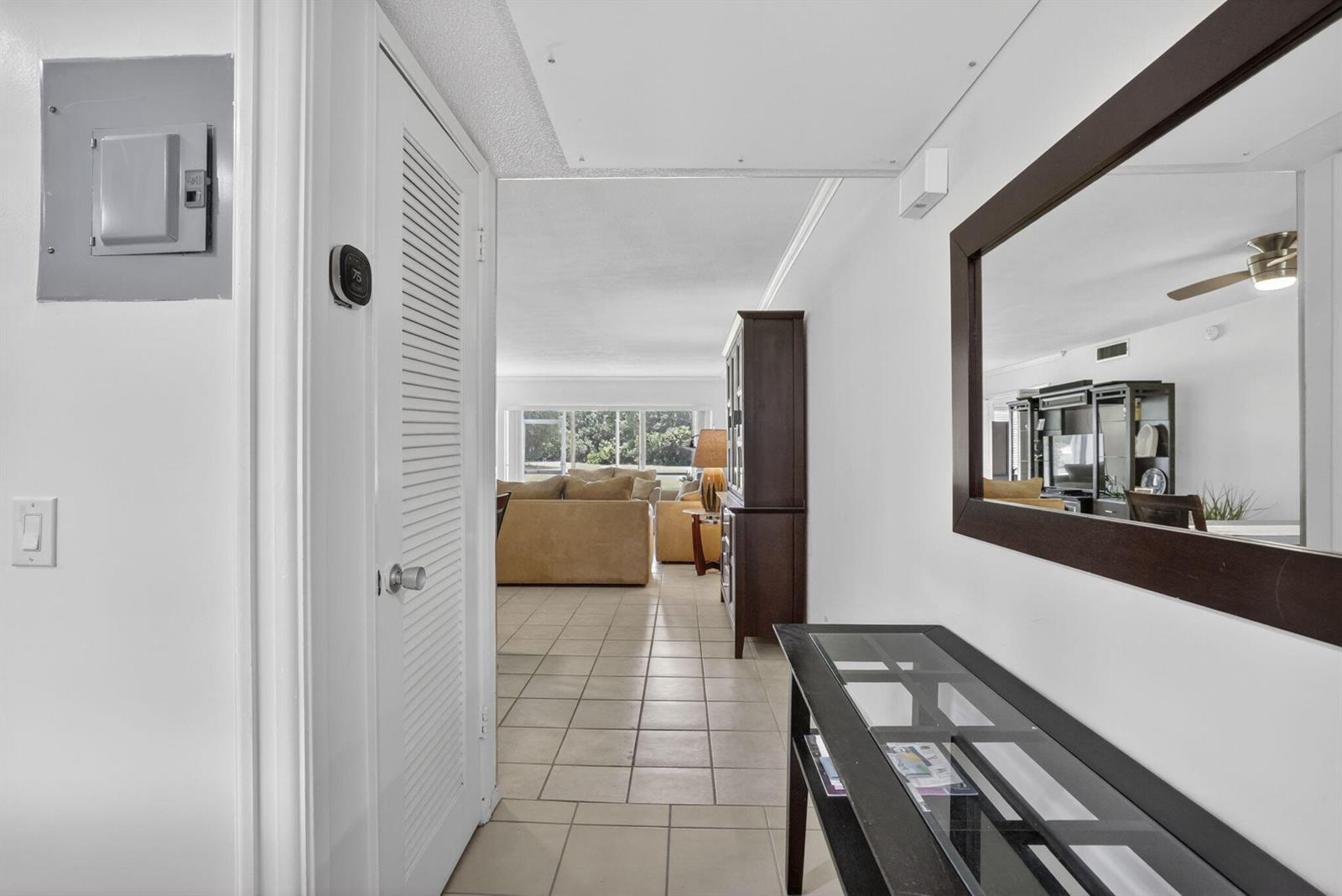 A hallway with a glass-topped console table and mirror leads to a tiled living area — 3150 N Palm Aire Drive # 108, Pompano Beach FL 33069, POMPANO BEACH, FL