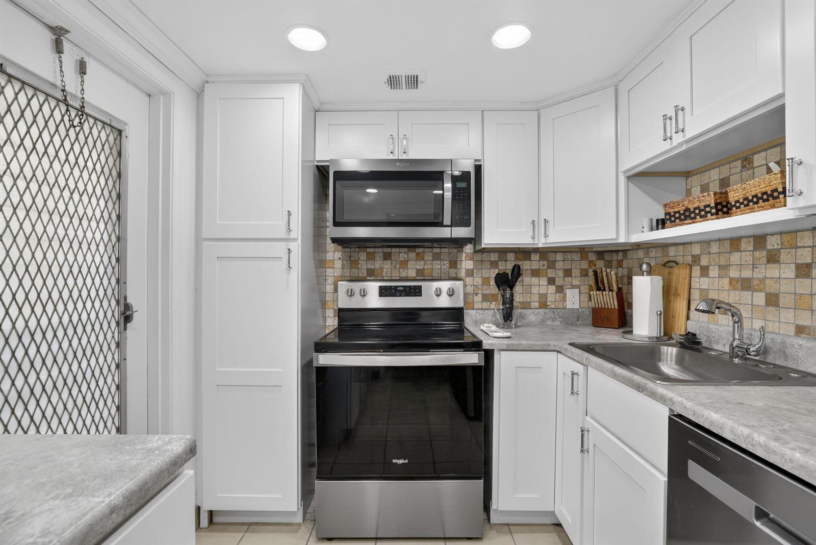 A kitchen features white cabinetry, stainless steel appliances, a tiled backsplash, and gray countertops — 3150 N Palm Aire Drive # 108, Pompano Beach FL 33069, POMPANO BEACH, FL