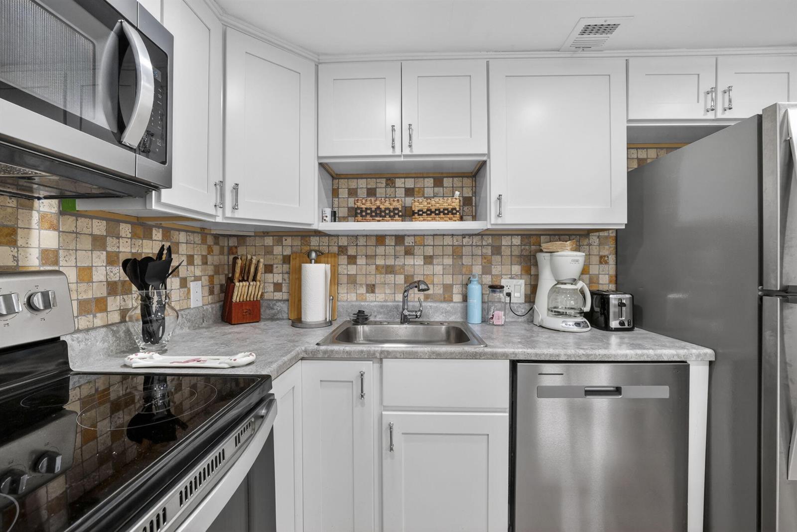 A kitchen with white cabinets, stainless steel appliances, a gray countertop, and a mosaic backsplash — 3150 N Palm Aire Drive # 108, Pompano Beach FL 33069, POMPANO BEACH, FL
