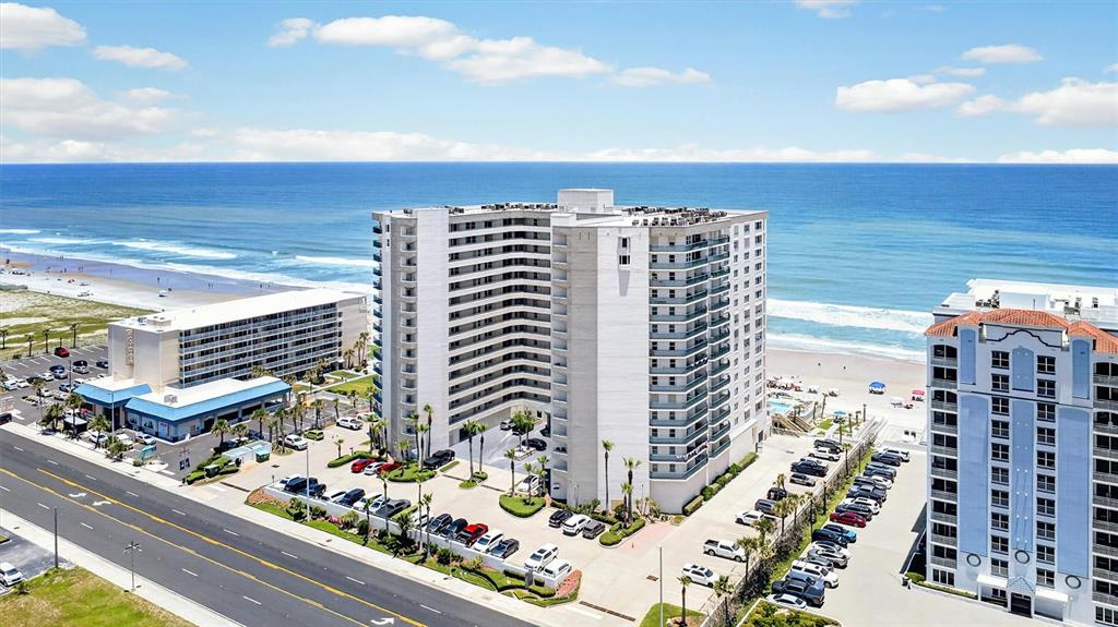 An aerial view shows a multi-story beachfront condominium complex with a parking lot — 2055 S ATLANTIC AVENUE UNIT 603, DAYTONA BEACH, FL