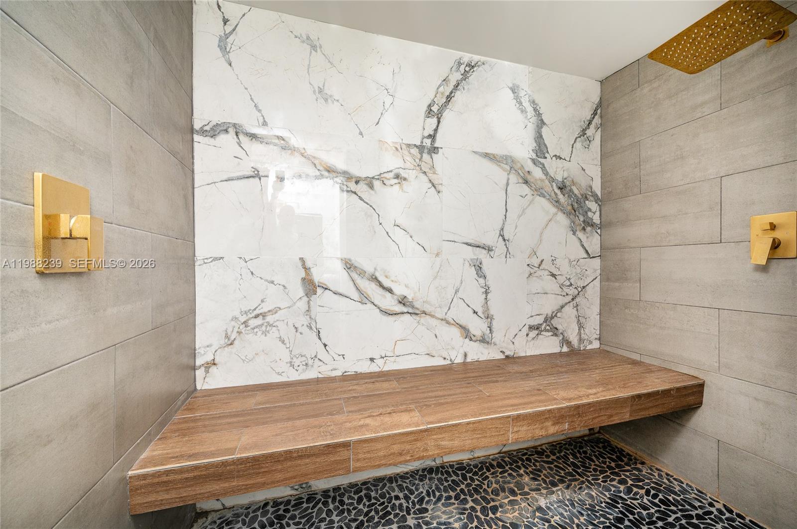 A shower features a wood-look bench, marble accent wall, gray tile, and gold fixtures — 10954 SW 157th Ter # 2, Miami FL 33157, MIAMI, FL
