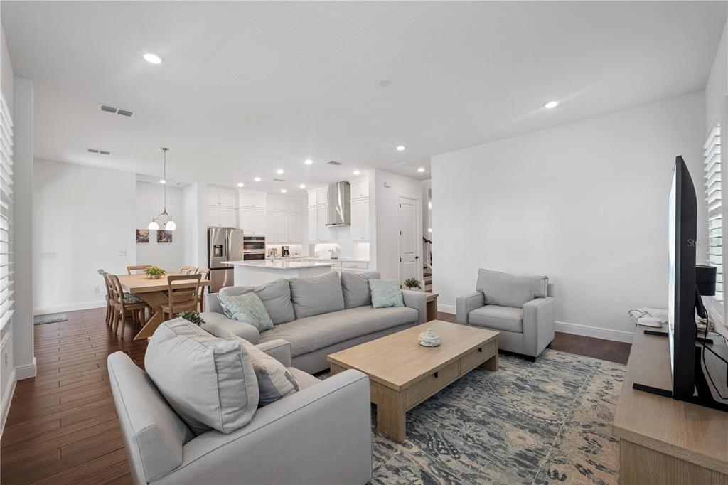 An open-concept living room and kitchen featuring light-colored furniture, hardwood floors, and white cabinetry — 17588 LAKE STAR ROAD, WINTER GARDEN, FL
