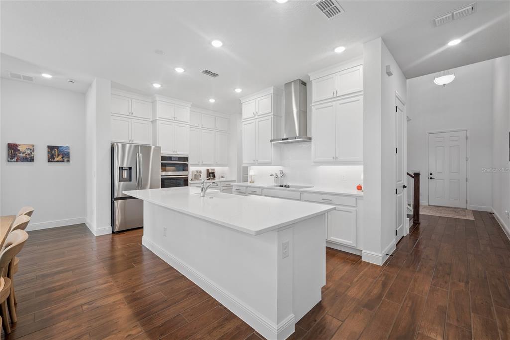 A modern kitchen features white cabinetry, a large quartz island, and dark wood flooring — 17588 LAKE STAR ROAD, WINTER GARDEN, FL
