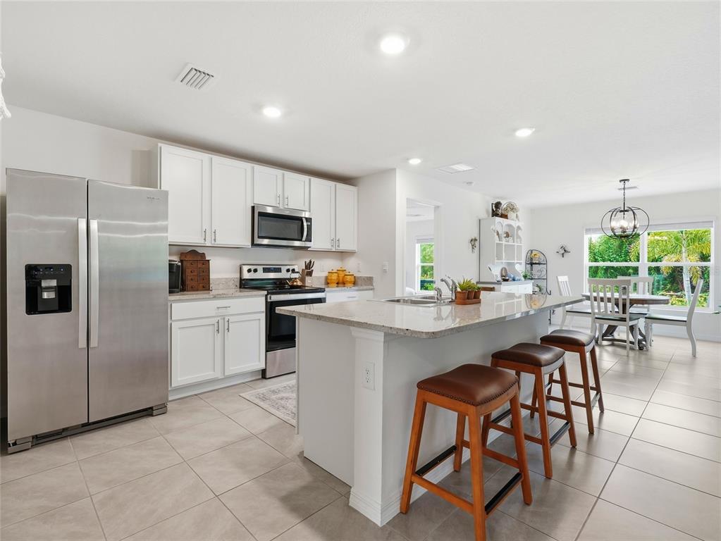 A kitchen features white cabinets, stainless steel appliances, a granite island, and tile flooring — 4419 HEARTHSTONE RUN, PALMETTO, FL