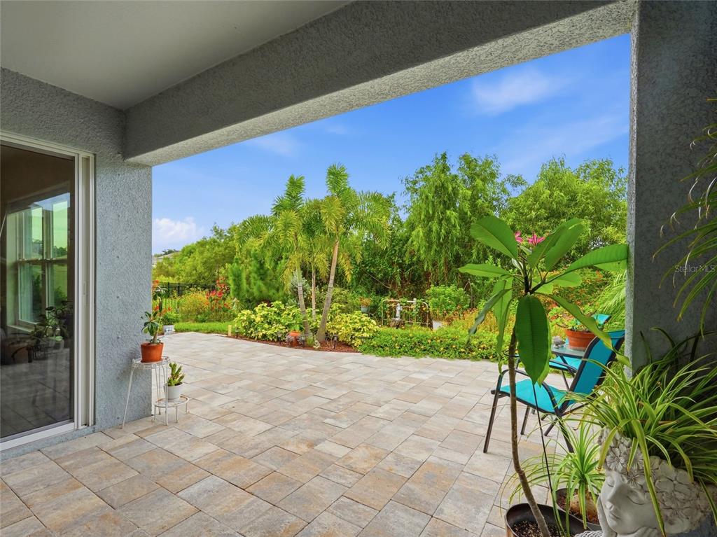 A covered patio with stone pavers overlooks a lush garden with palm trees and greenery — 4419 HEARTHSTONE RUN, PALMETTO, FL