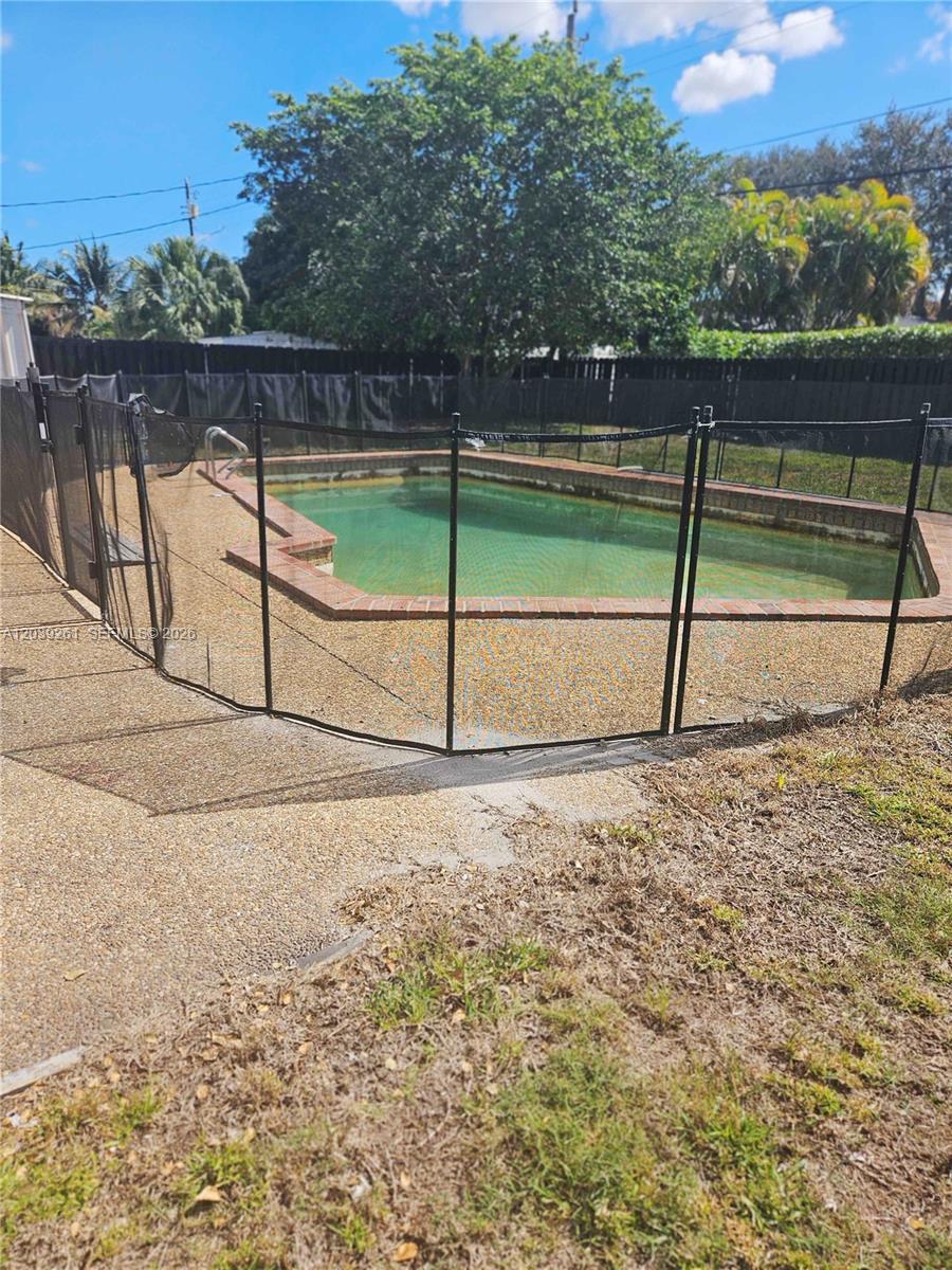 An outdoor swimming pool with a brick border is enclosed by a black mesh fence — 4506 Taft St, Hollywood FL 33021, HOLLYWOOD, FL