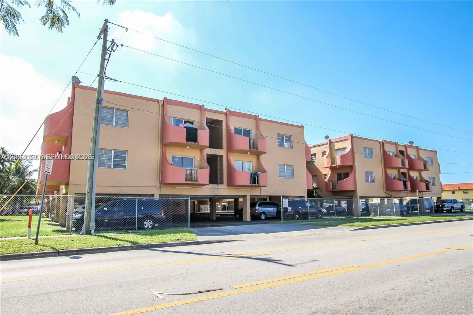 A multi-story apartment building features tan stucco walls, pink balconies, and ground-level covered parking — 3675 W 11th Ave # 319, Hialeah FL 33012, HIALEAH, FL