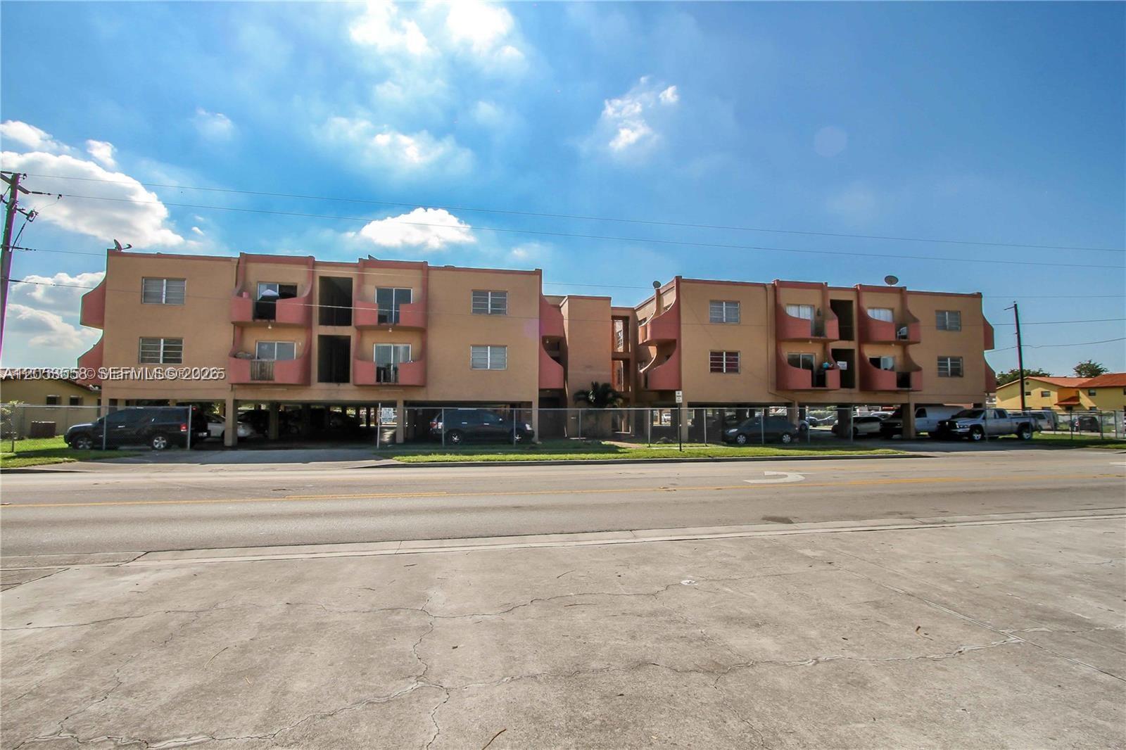 A three-story apartment building with covered ground-level parking sits behind a chain-link fence — 3675 W 11th Ave # 319, Hialeah FL 33012, HIALEAH, FL