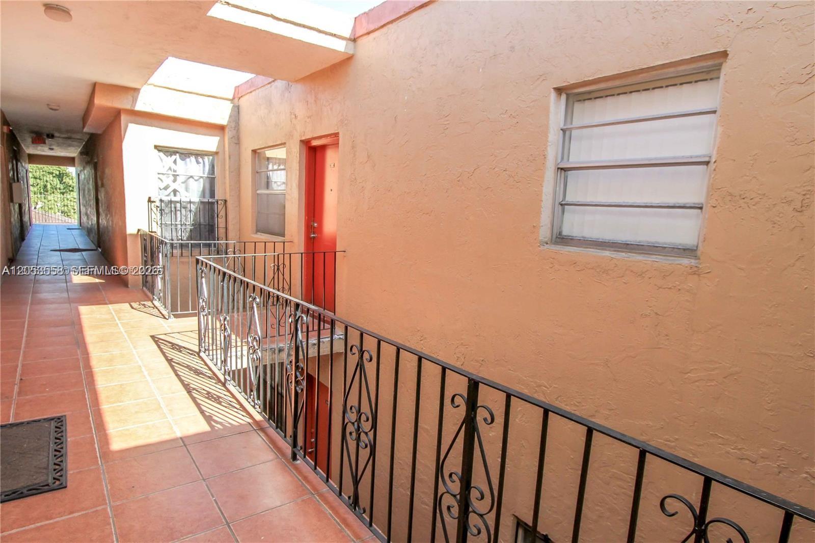An outdoor walkway with tile flooring, a metal railing, and a red door — 3675 W 11th Ave # 319, Hialeah FL 33012, HIALEAH, FL