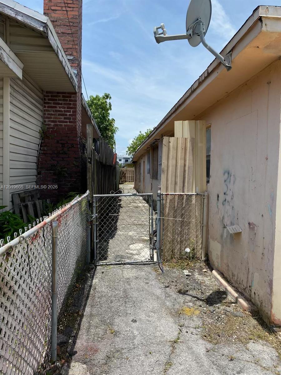 A narrow concrete walkway sits between two buildings, separated by a chain-link fence and gate — 2640 NW 23rd Ct, Miami FL 33142, MIAMI, FL