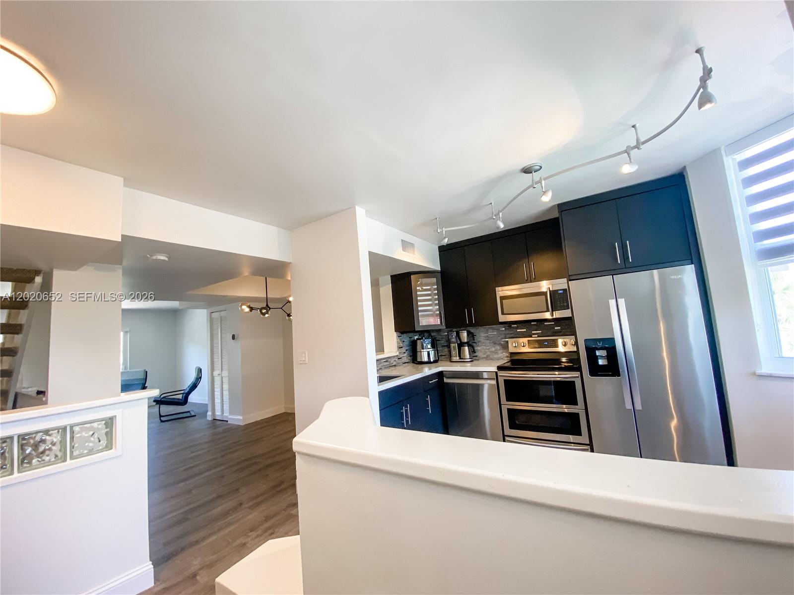 A kitchen with dark cabinets and stainless steel appliances overlooks an open living area — 8661 NW 4th Ter # 903, Miami FL 33126, MIAMI, FL
