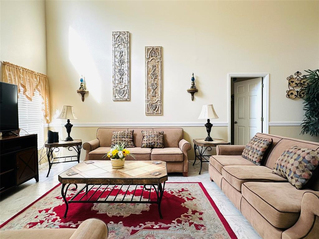 A living room features two tan sofas, a central coffee table, and decorative wall panels — 1049 LAKE BERKLEY DRIVE, KISSIMMEE, FL
