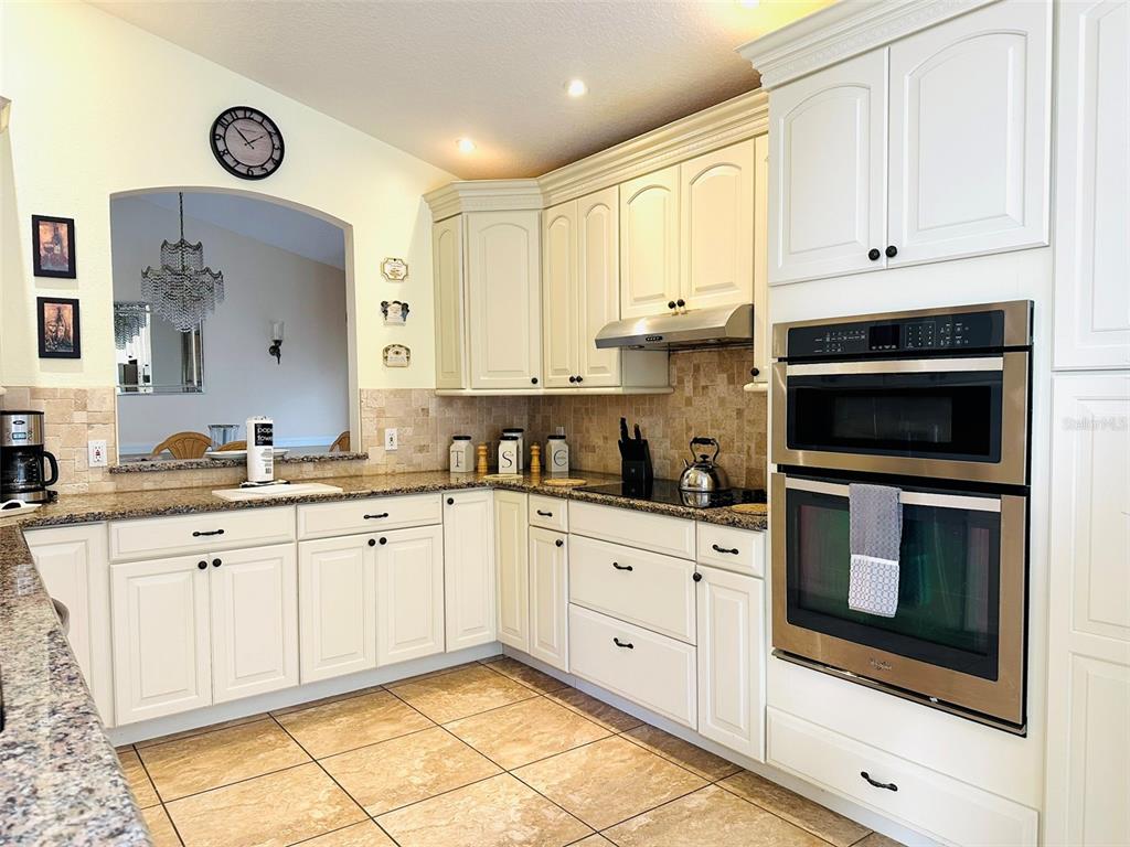 A kitchen features white cabinetry, granite countertops, stainless steel appliances, and tile flooring — 1049 LAKE BERKLEY DRIVE, KISSIMMEE, FL