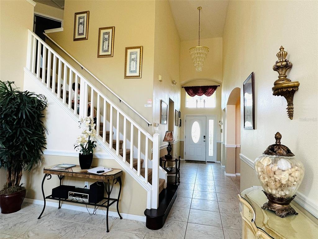 A bright foyer features a staircase with white railings, tile flooring, and a chandelier — 1049 LAKE BERKLEY DRIVE, KISSIMMEE, FL