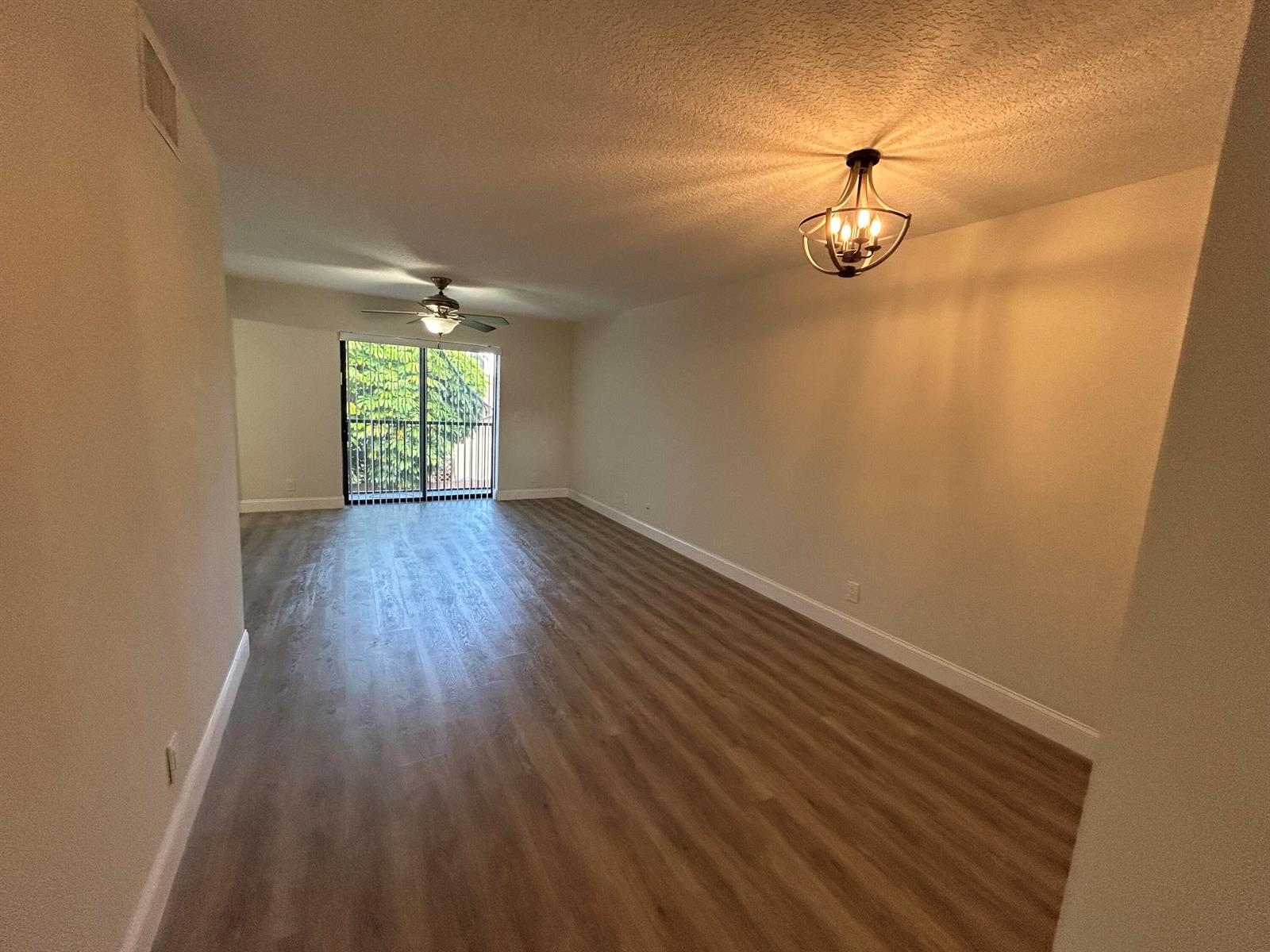 An empty living room features wood-look flooring, a ceiling fan, and a sliding glass door — 21906 Lake Forest Circle, Boca Raton FL 33433, BOCA RATON, FL