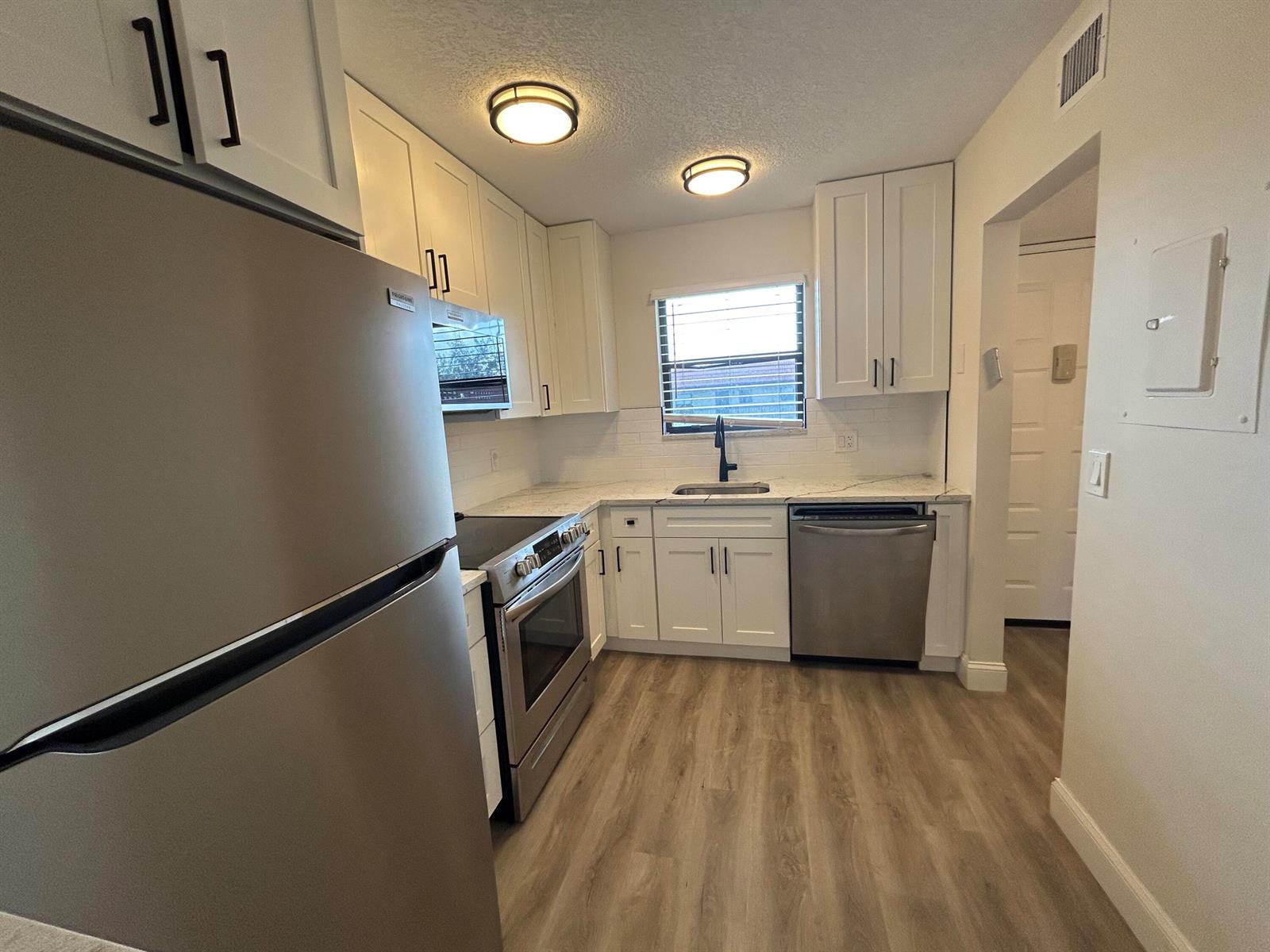A kitchen features white cabinets, stainless steel appliances, a window, and light wood-look flooring — 21906 Lake Forest Circle, Boca Raton FL 33433, BOCA RATON, FL