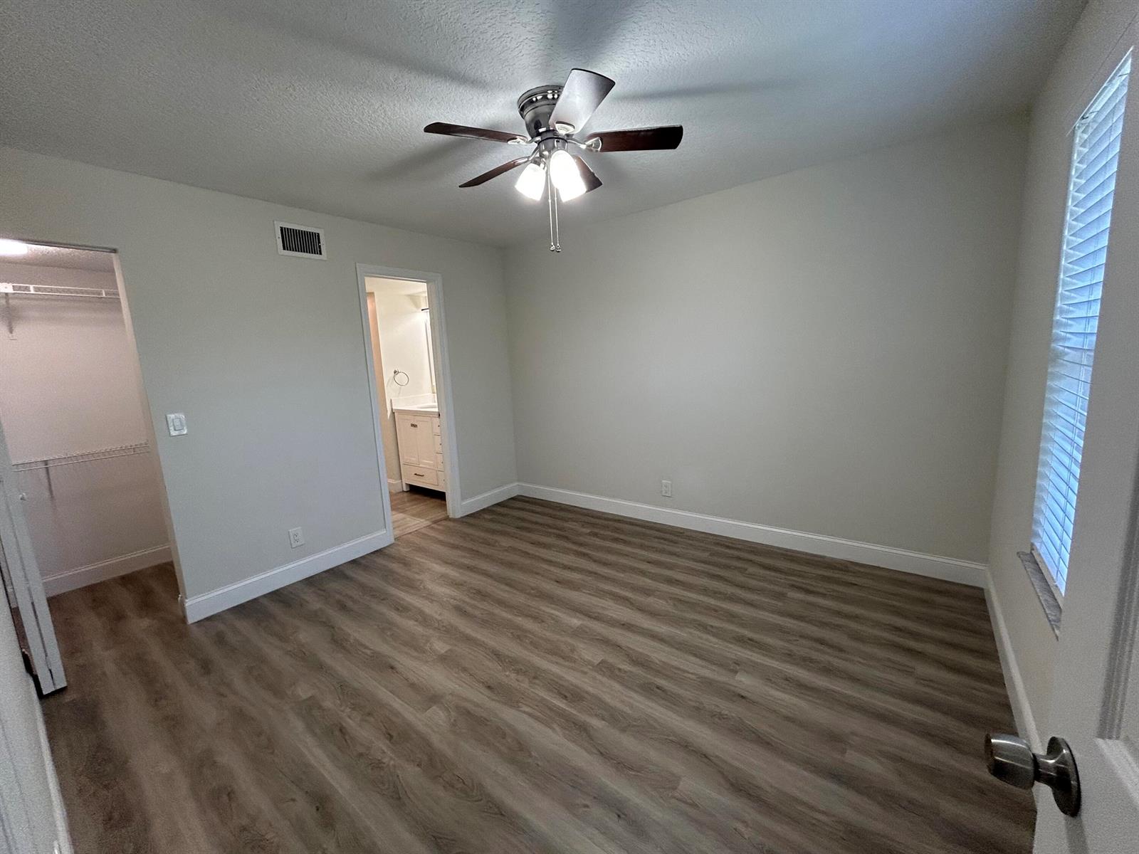 An empty bedroom features light gray walls, wood-look flooring, a ceiling fan, and an attached bathroom — 21906 Lake Forest Circle, Boca Raton FL 33433, BOCA RATON, FL