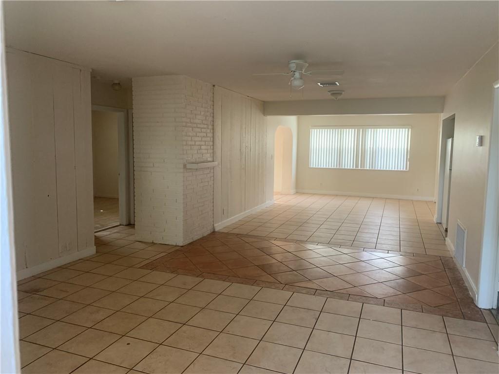 An open-concept living area features white-painted brick, wood-paneled walls, and light-colored tile flooring — 6410 Coolidge Street, Hollywood FL 33024, HOLLYWOOD, FL