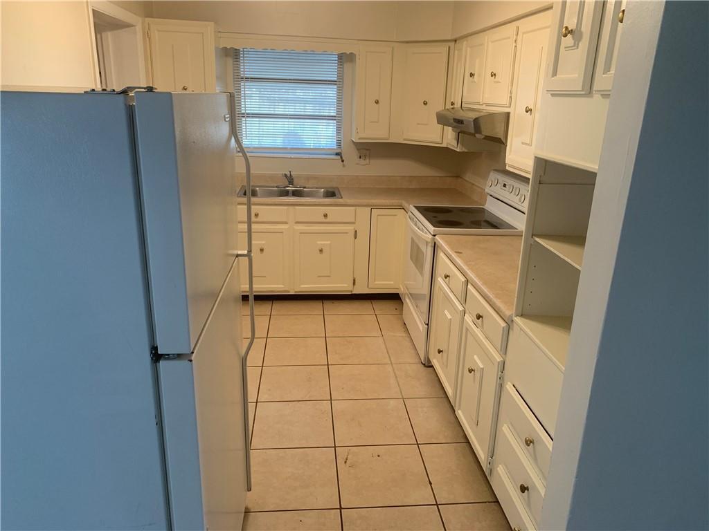 A kitchen features white cabinets, a white refrigerator, a stove, and light-colored tile flooring — 6410 Coolidge Street, Hollywood FL 33024, HOLLYWOOD, FL