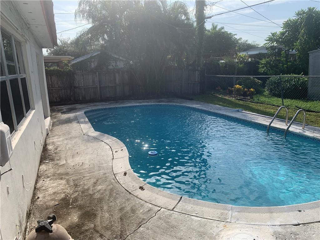 A backyard swimming pool with a concrete deck is enclosed by a wooden fence — 6410 Coolidge Street, Hollywood FL 33024, HOLLYWOOD, FL