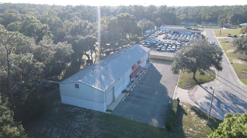An aerial view shows a metal-roofed commercial building with a parking lot and surrounding trees — 3710 NE 47TH PLACE, OCALA, FL