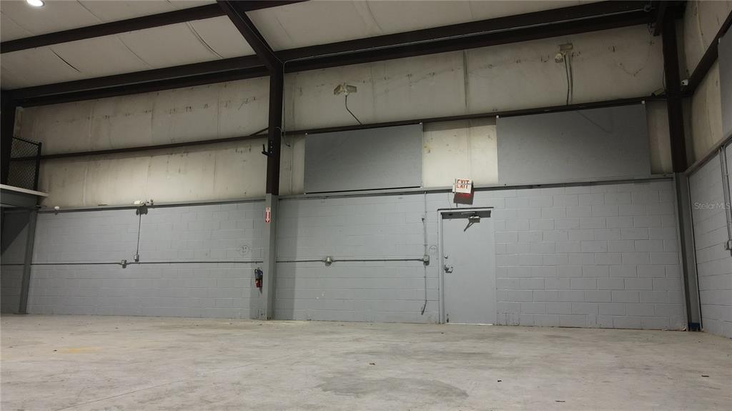An interior view of a warehouse space with gray concrete block walls and a door — 3710 NE 47TH PLACE, OCALA, FL
