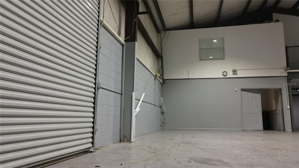 An interior view of a warehouse space with a roll-up door and a loft area — 3710 NE 47TH PLACE, OCALA, FL