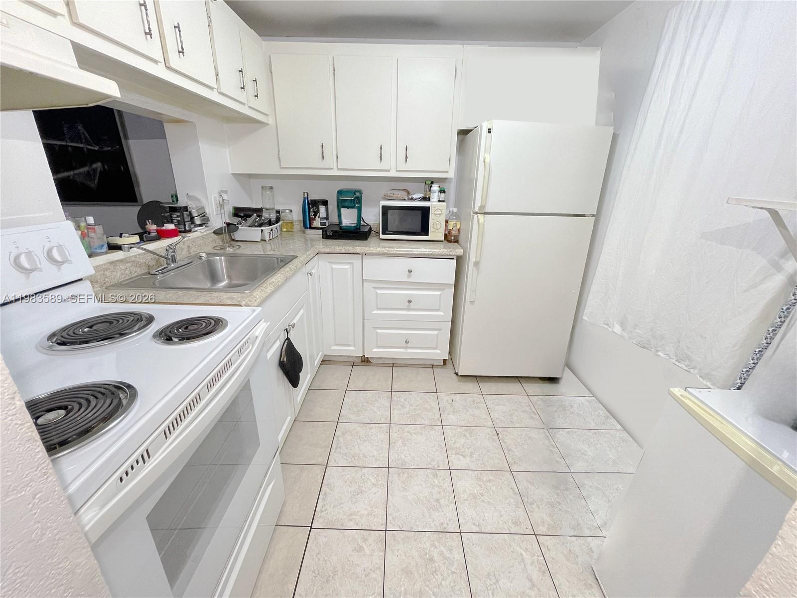 A kitchen features white cabinets, white appliances, a stainless steel sink, and light tile flooring — 2800 NW 56th Ave # E103, Lauderhill FL 33313, LAUDERHILL, FL