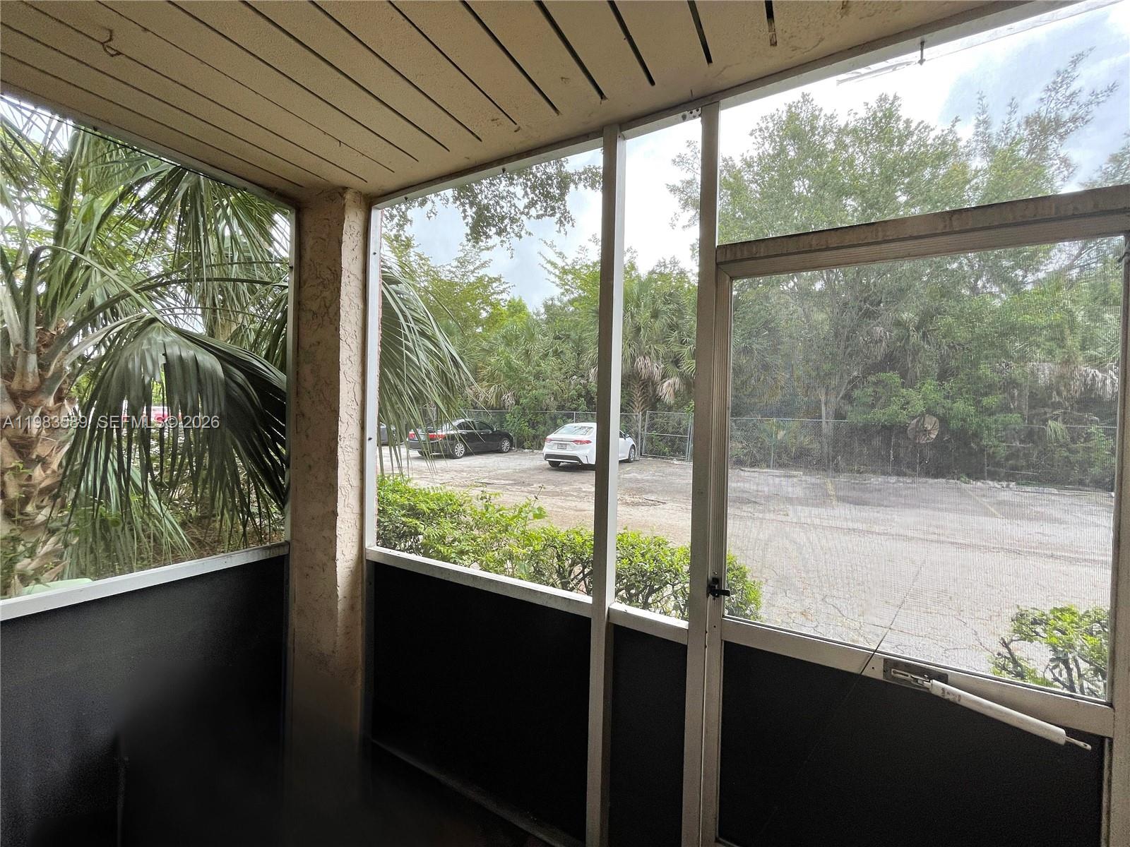 A screened-in porch overlooks a parking lot with two cars and surrounding trees — 2800 NW 56th Ave # E103, Lauderhill FL 33313, LAUDERHILL, FL