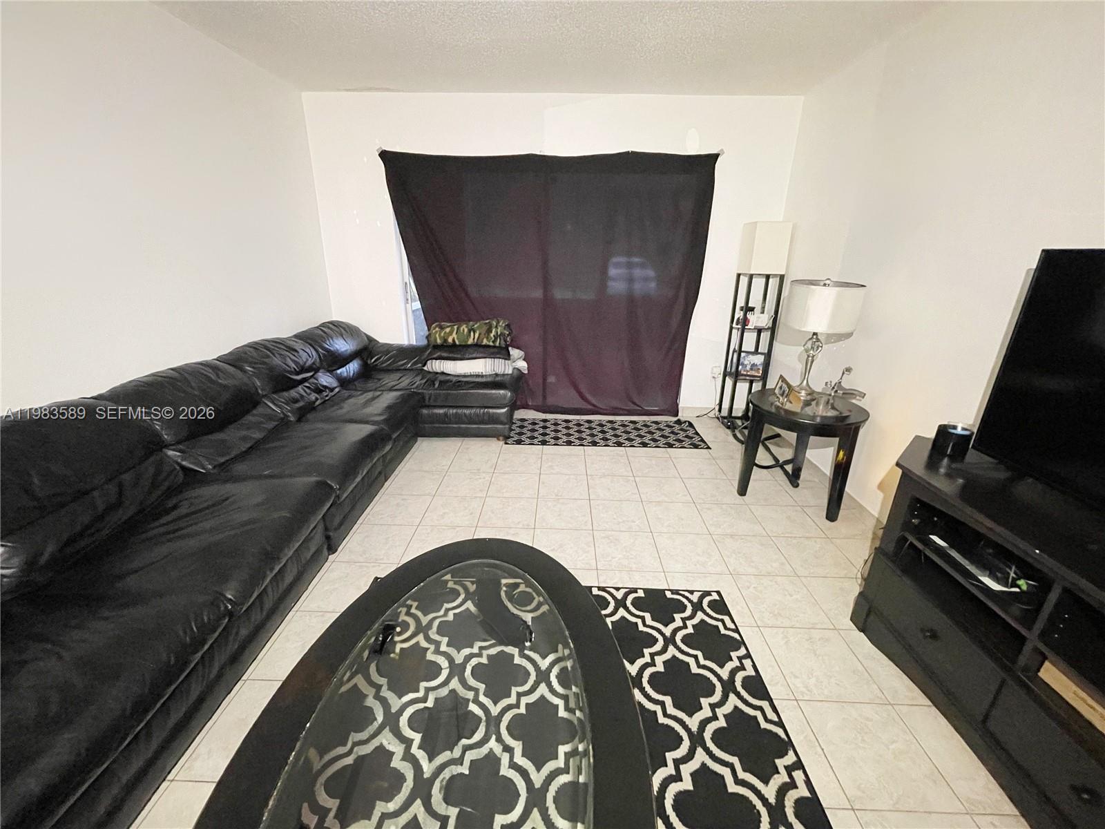 A living room features a black sectional sofa, tiled floors, and a patterned area rug — 2800 NW 56th Ave # E103, Lauderhill FL 33313, LAUDERHILL, FL