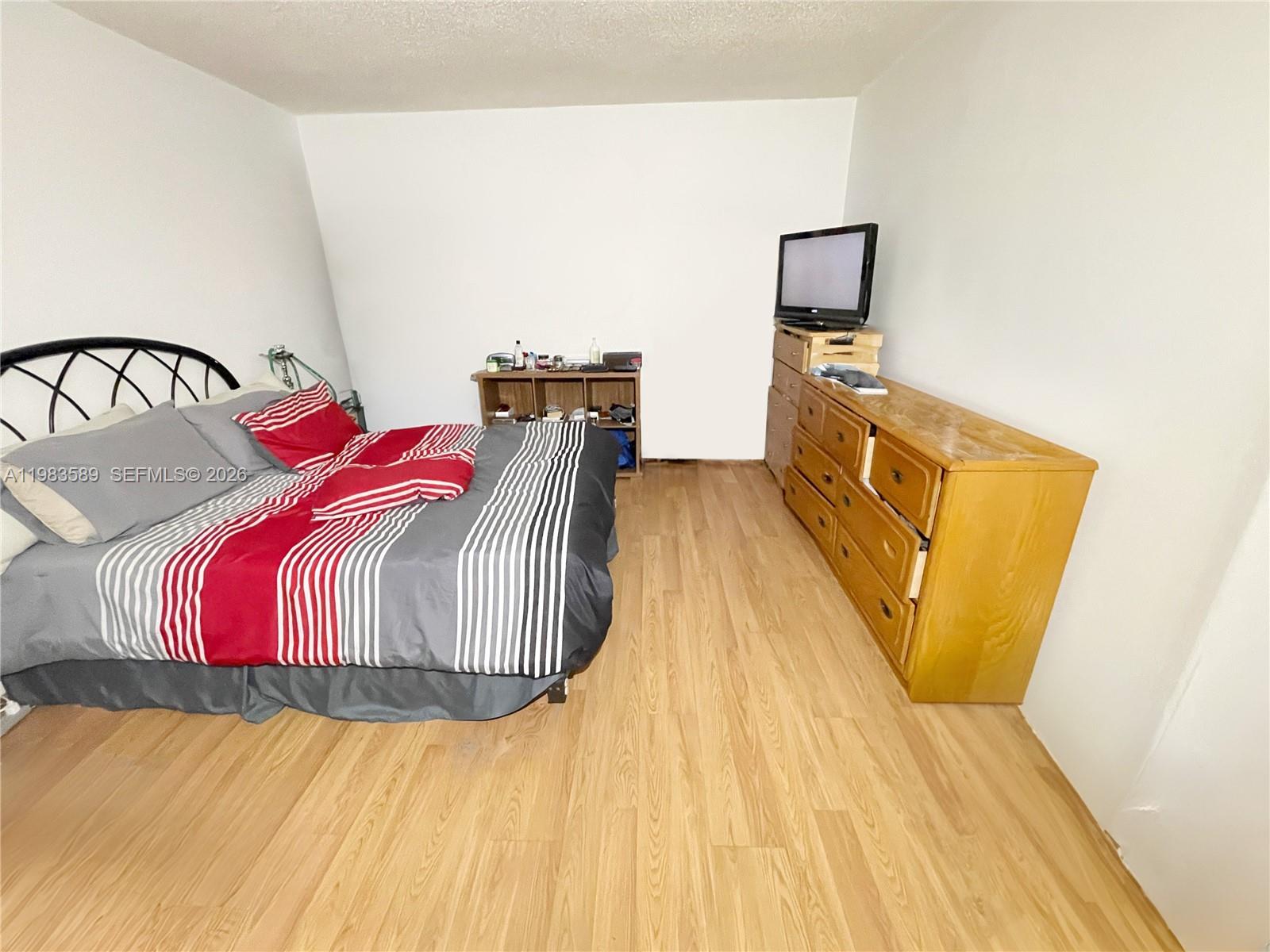 A bedroom features a bed with striped bedding, a wooden dresser, and light wood flooring — 2800 NW 56th Ave # E103, Lauderhill FL 33313, LAUDERHILL, FL