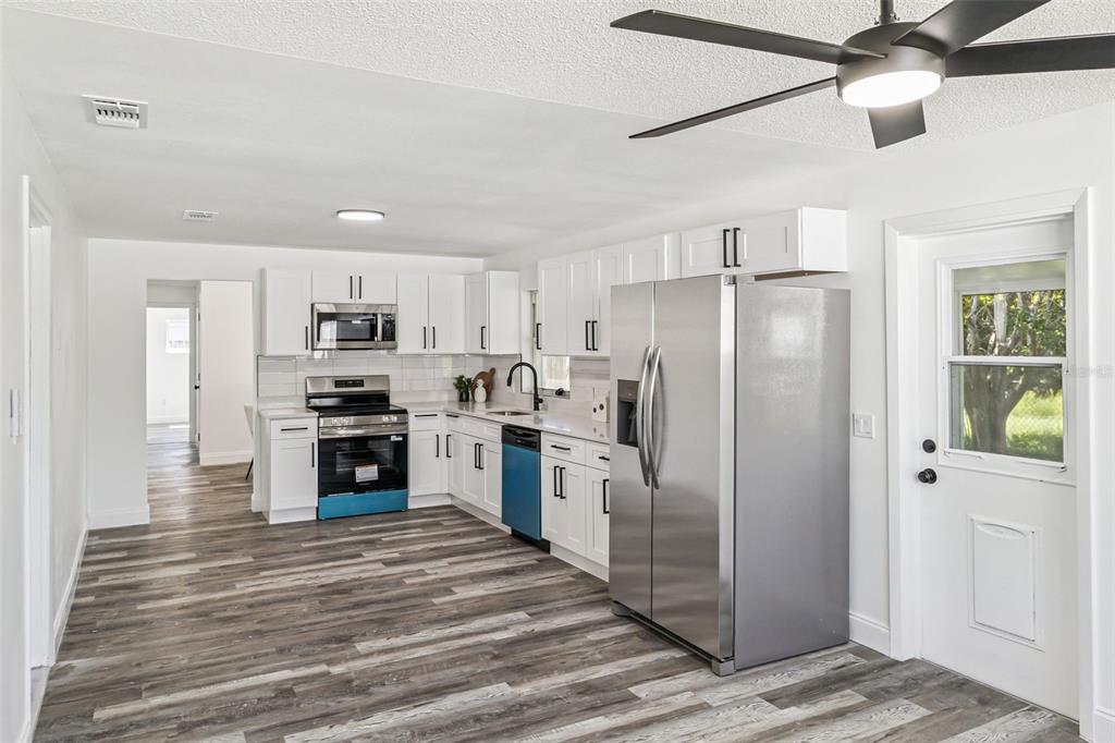 A kitchen features white cabinets, stainless steel appliances, and wood-look flooring under a ceiling fan — 903 JEFFERSON ROAD, ROCKLEDGE, FL